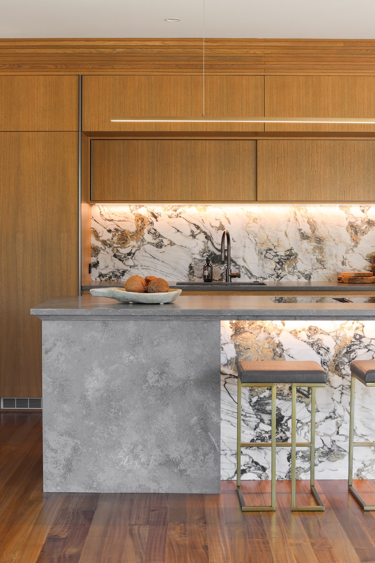 kitchen island with marble splashback and veneer timber cabinetry in a warm stain